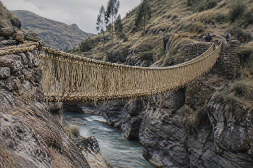 A woven rope bridge deck viewed from the rocky bank of a river gorge