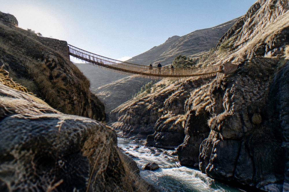 A river running through a deep gorge below a rope bridge in the Andes
