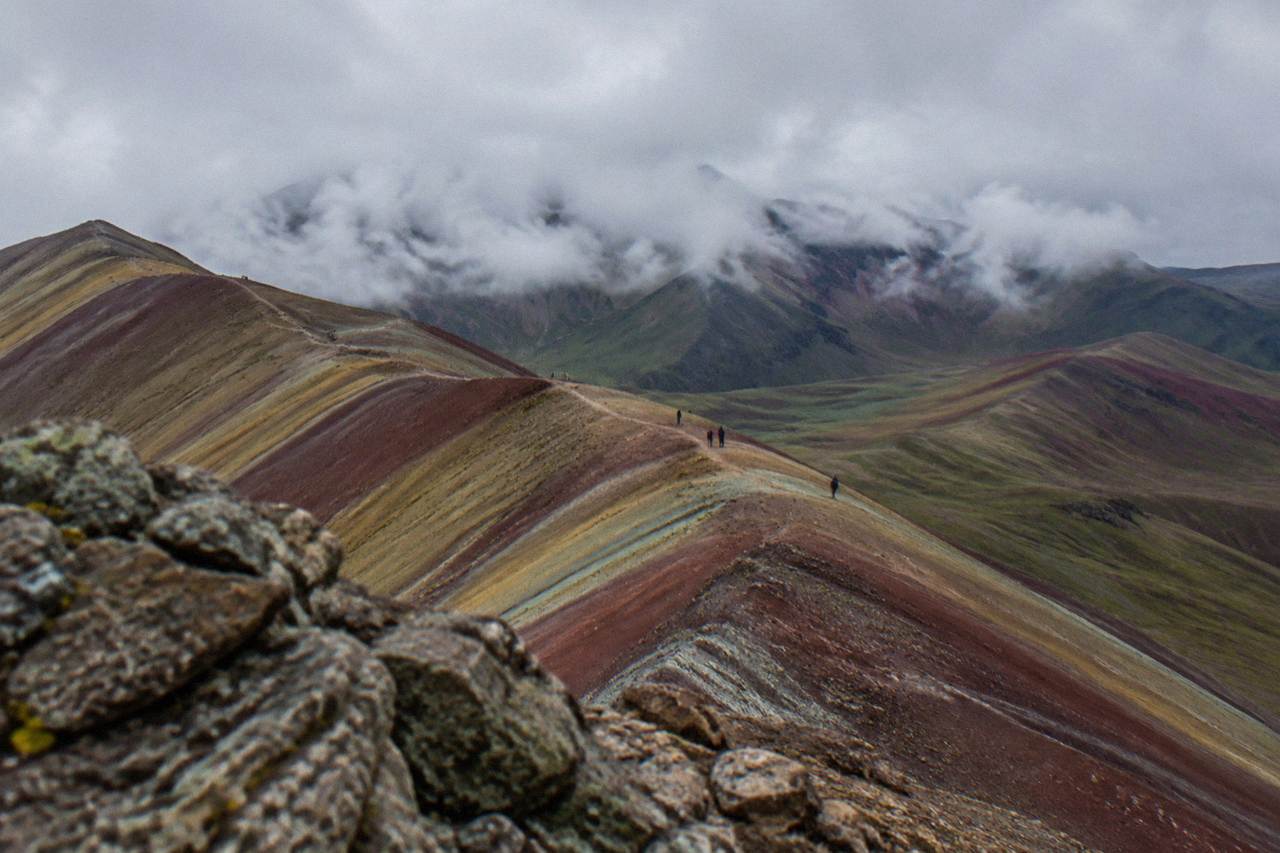 Striped red and gold mountain slopes under a wide Andean sky with a dirt trail crossing the ridge