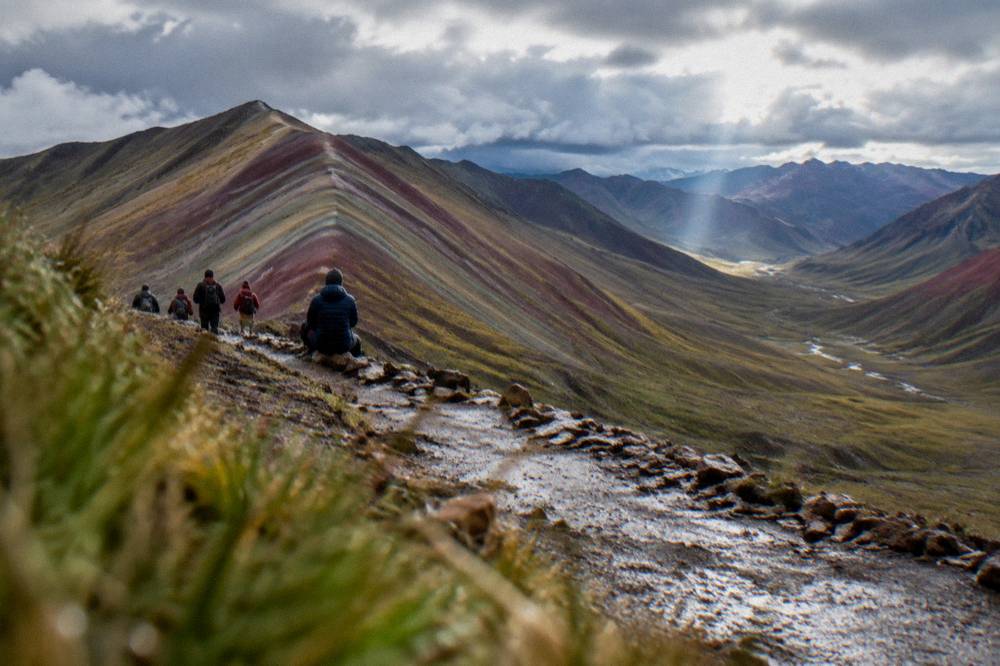 Walkers in warm jackets and hats resting on a high trail with wide valley views below