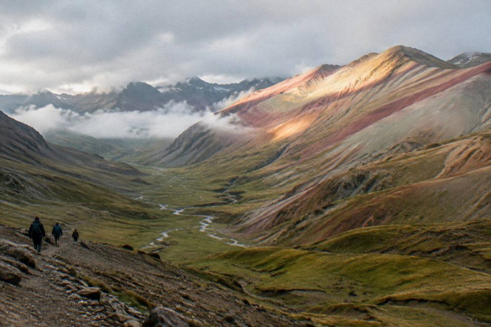 Sunrise light on layered pink and ochre mountain bands with a valley of streams below