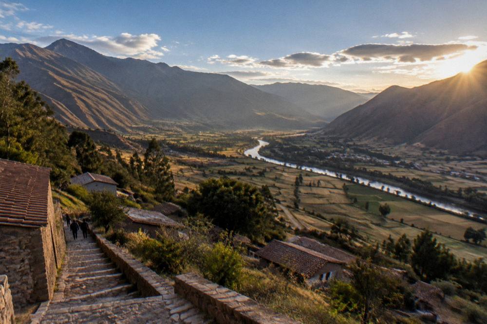 A wide panorama of the Sacred Valley with the river winding between farmland and mountains at golden hour