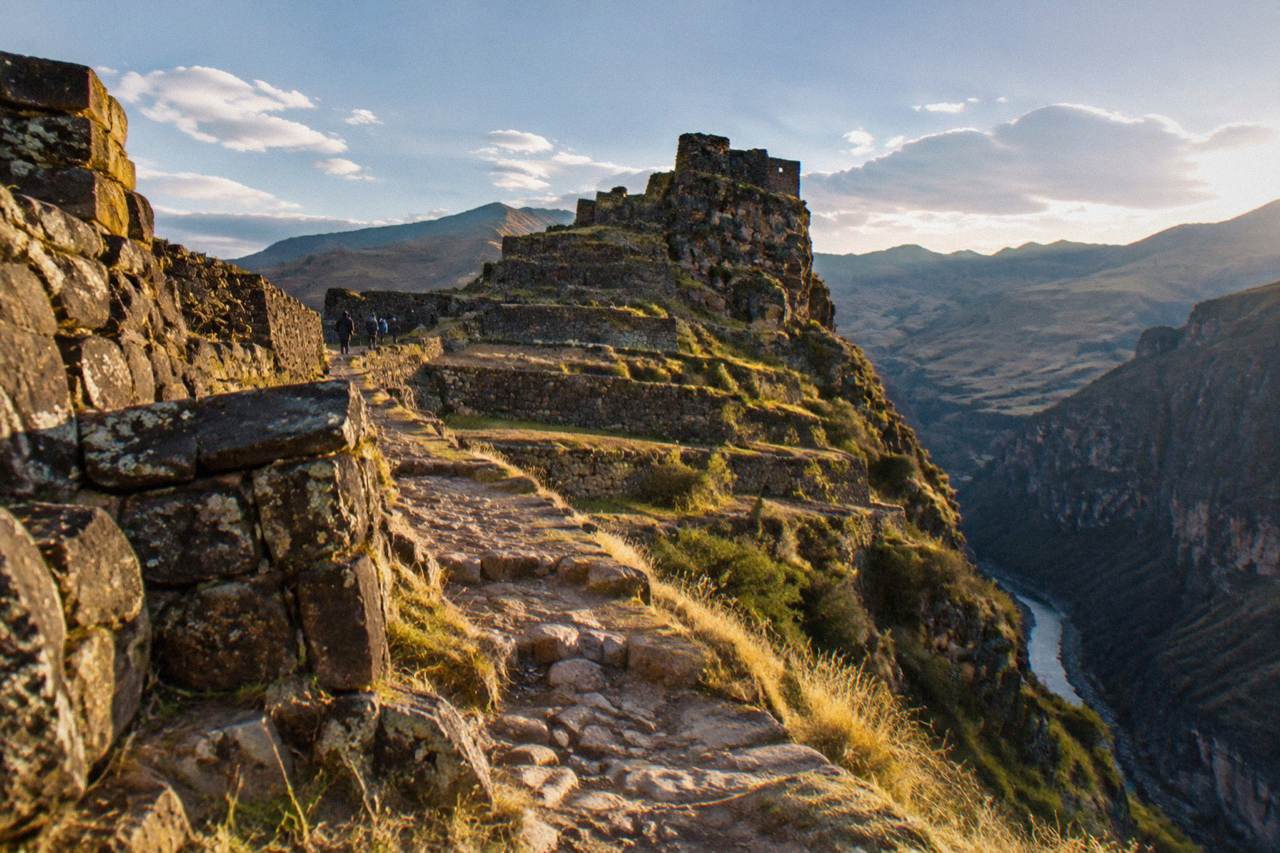 Stone Inca terraces and walls built onto a rocky ridge above a river canyon in the Andes near Cusco
