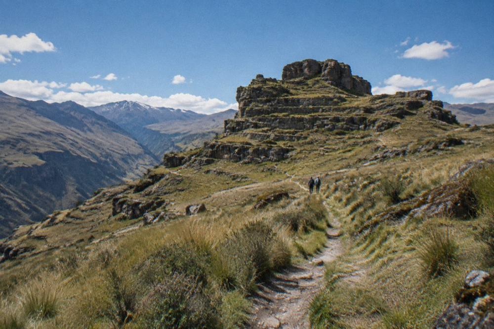 A narrow footpath winding across high grassland toward a rocky outcrop in the Peruvian Andes