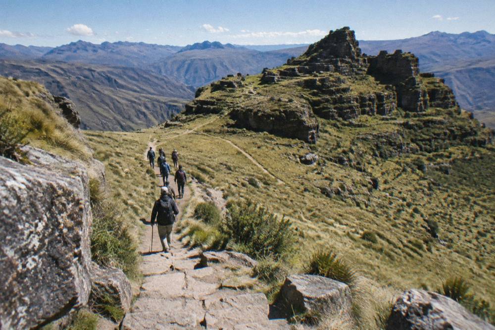 A guided group of hikers walking a dirt trail through open Andean grassland