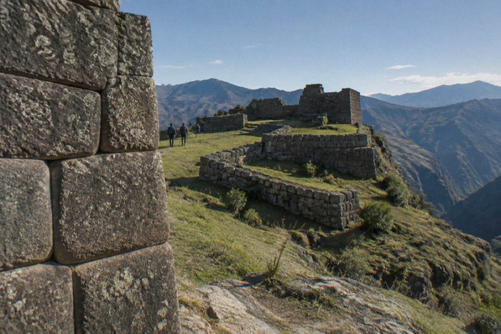 Inca stone walls with precisely fitted blocks standing on a grassy ridge under a blue sky