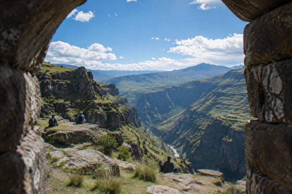 Hikers resting on a rocky ledge with wide views over a green river canyon in the Andes