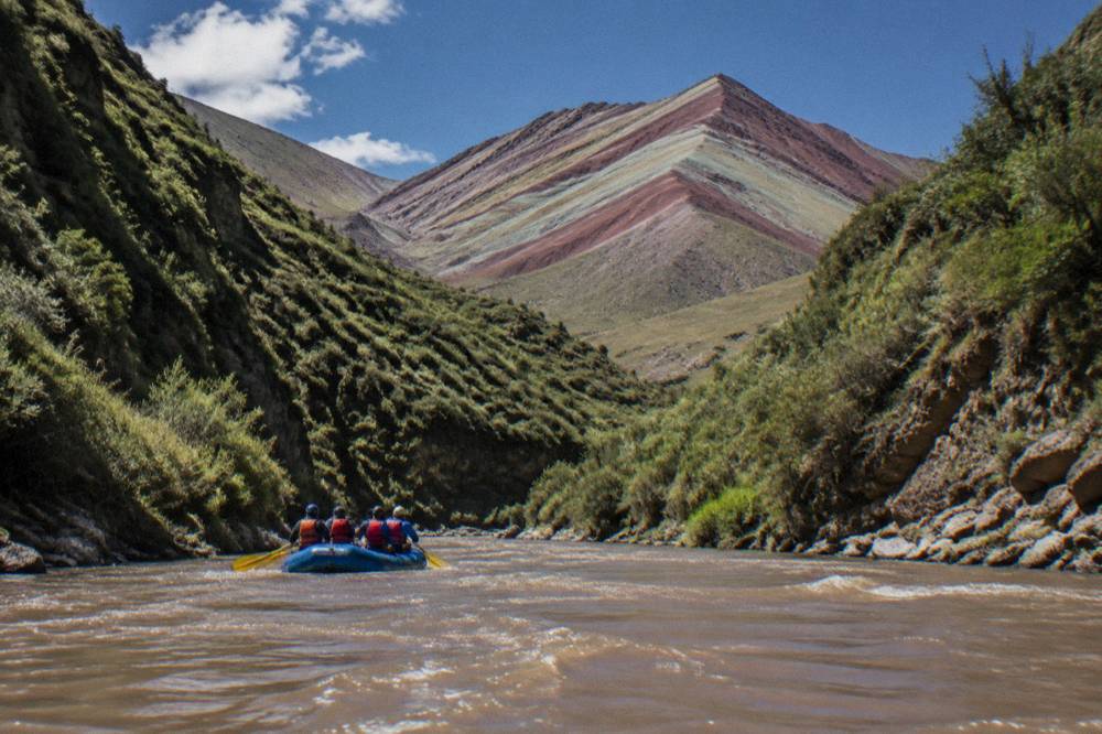 A raft with paddlers on a brown Andean river between steep green banks