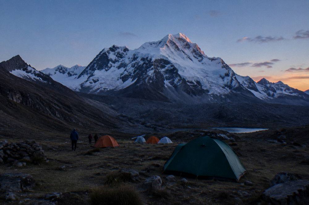 Trekkers with a small camp below a snow-covered Andean peak at dawn