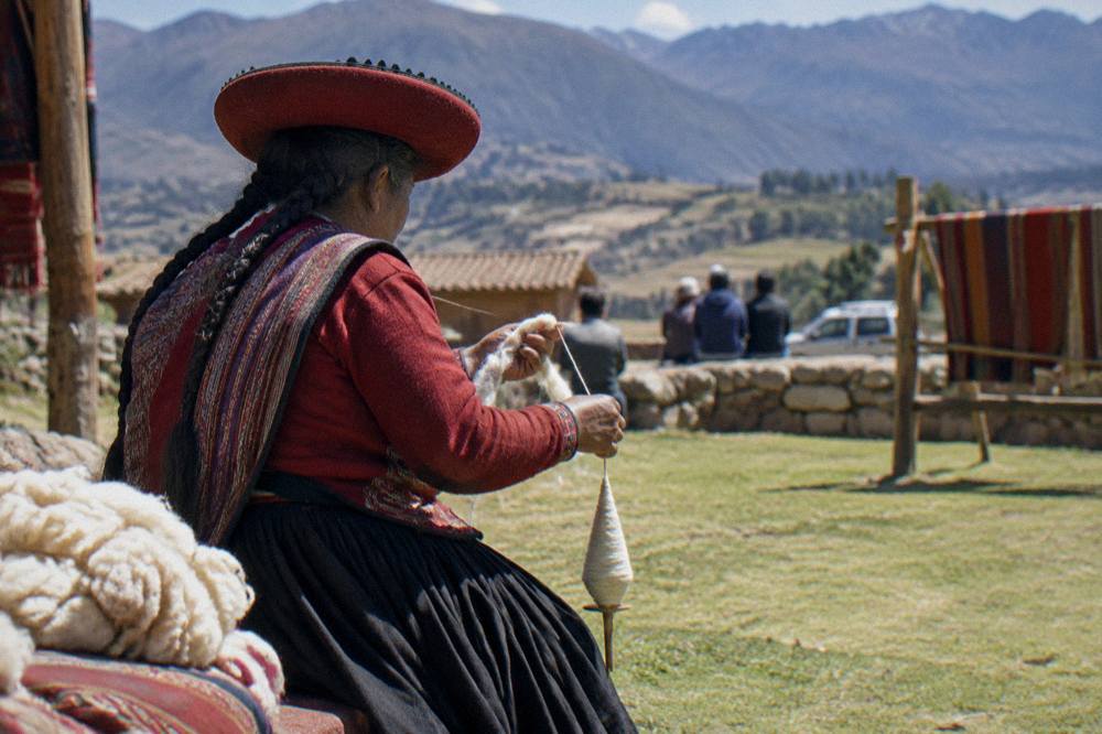 A weaver in traditional dress spinning yarn by hand at a community weaving demonstration