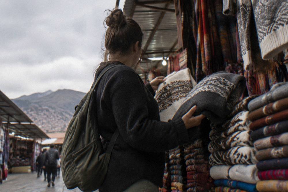 A shopper comparing two folded sweaters at a textile stall in Cusco
