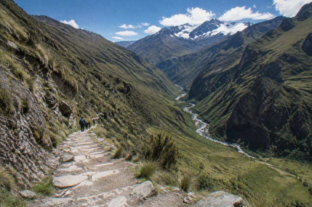 Trekking path descending steeply into a deep green canyon with a river visible far below