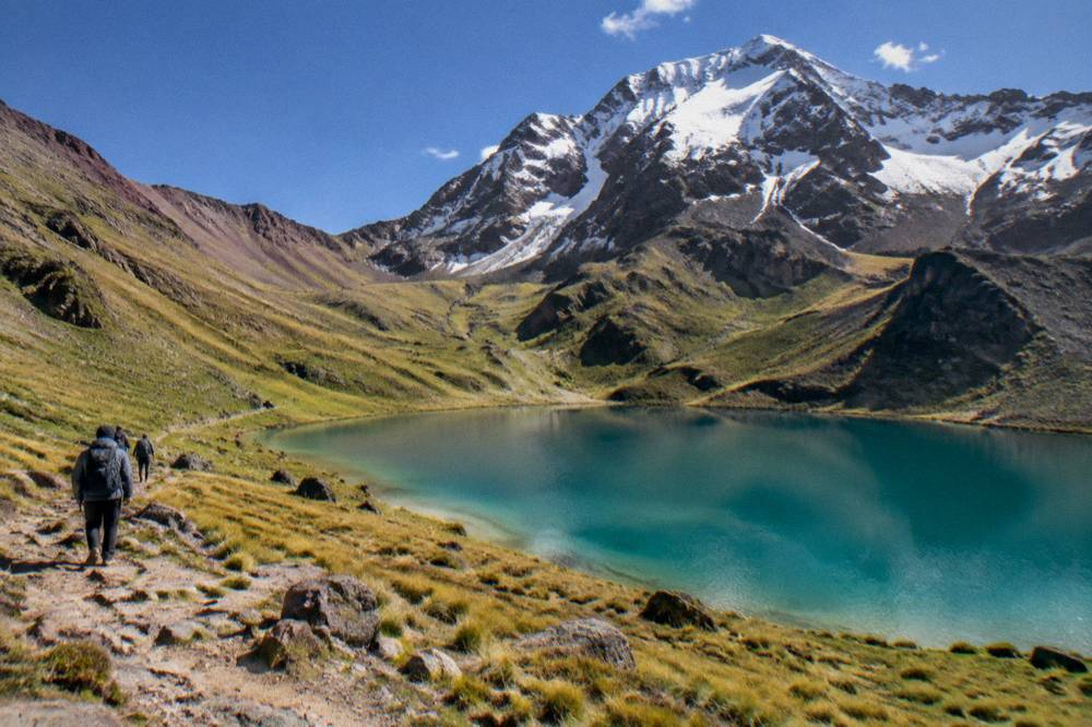 A turquoise mountain lake ringed by grassy slopes below a snow-dusted peak