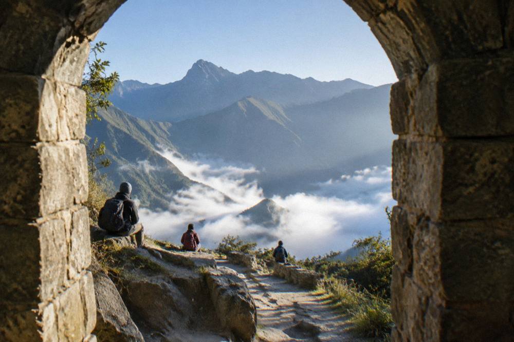Trekkers with backpacks resting on a high mountain path above morning cloud in a deep valley