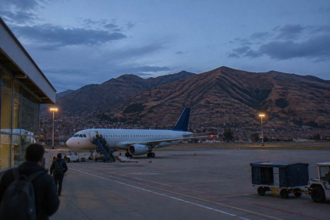 A small Andean city airport with a parked aircraft and dry brown hills rising behind the runway