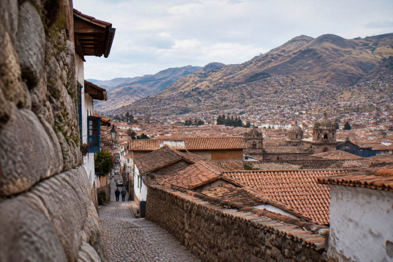 Terracotta rooftops of Cusco spreading across a high Andean valley with dry hillsides rising under a bright sky