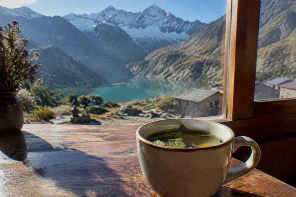 A cup of coca tea resting on a wooden table beside a window overlooking Cusco rooftops