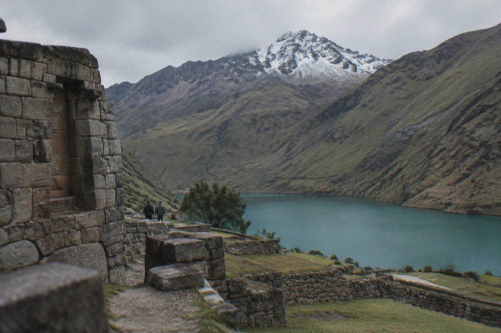 A turquoise mountain lake ringed by steep grassy slopes and a snow dusted peak