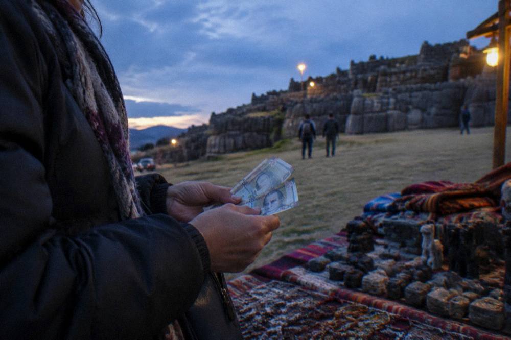 A visitor counting Peruvian sol banknotes at a market stall