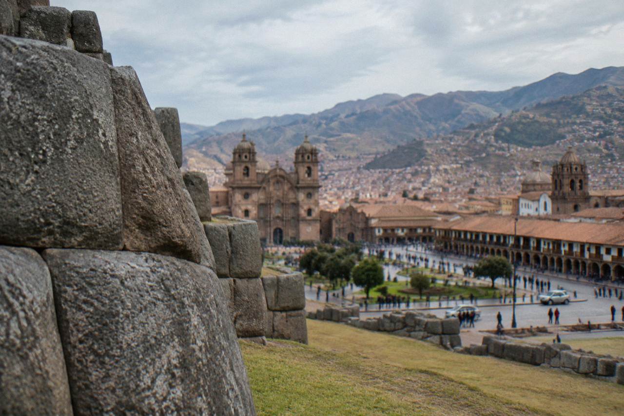 A crowded plaza in Cusco with colonial arcades and church towers under an Andean sky
