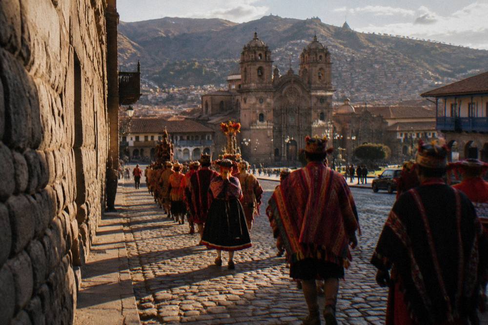 Performers in traditional dress processing through a stone-walled Andean street