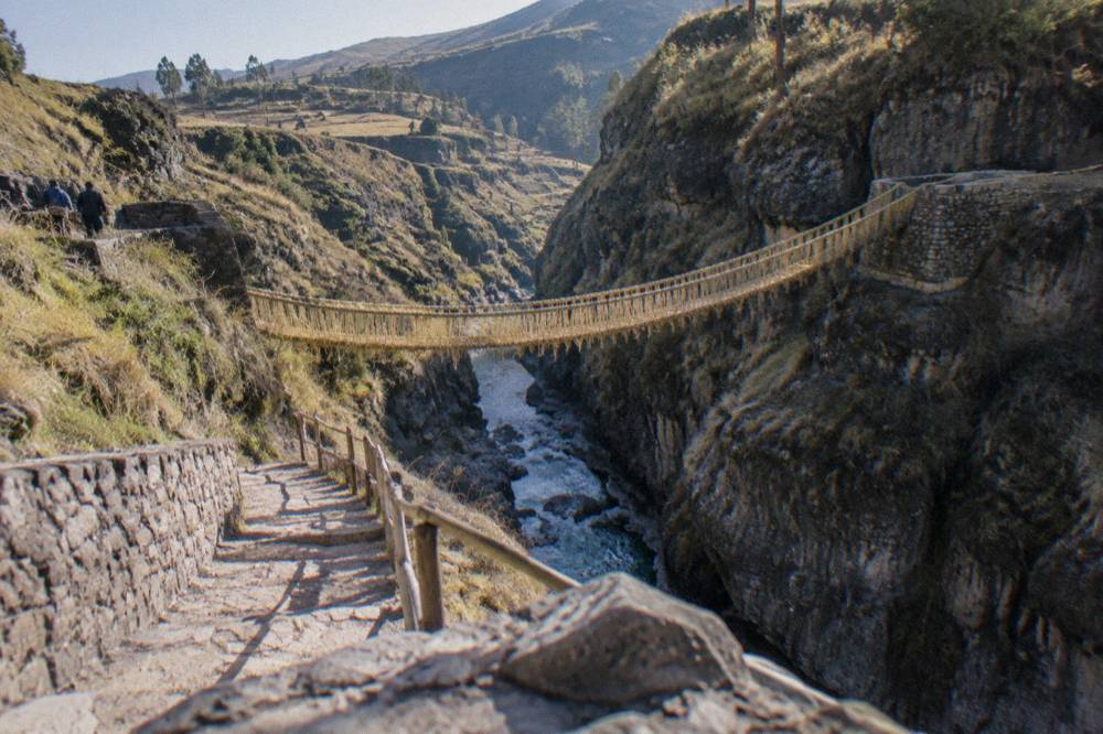 A woven grass rope bridge spanning a deep river gorge in the Andes