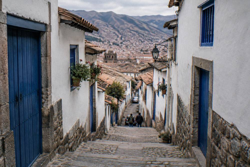A steep narrow street in the San Blas quarter of Cusco with whitewashed walls and blue doors