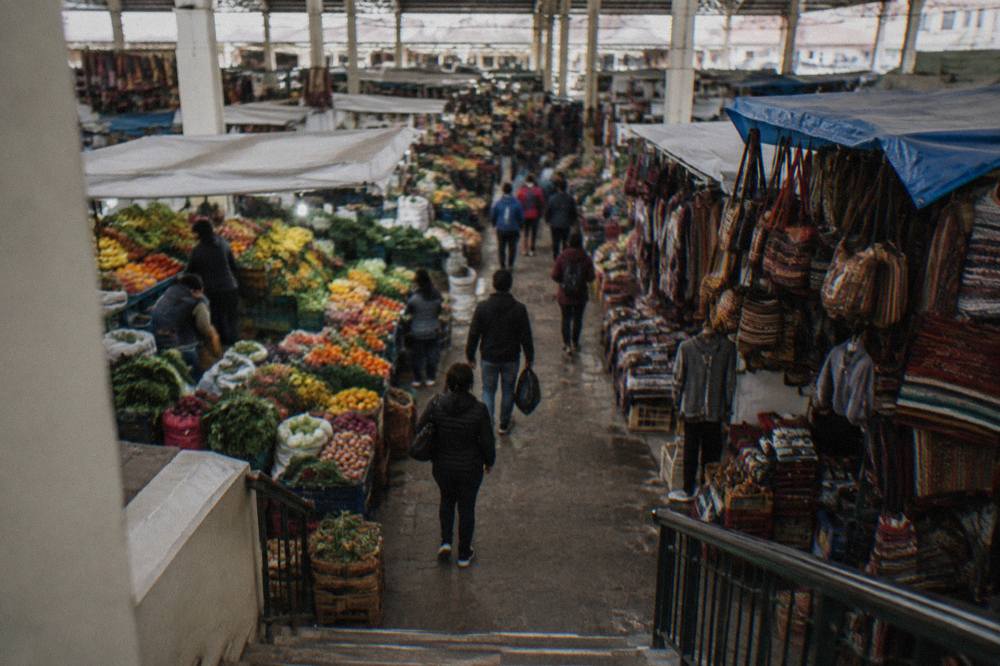 A busy market aisle in Cusco with shoppers between stalls under the hall's roof