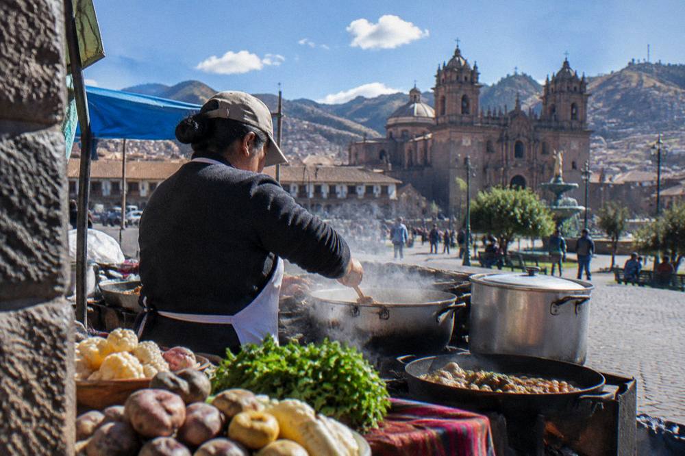 A cook preparing Andean dishes at a market stove with steam rising from pots