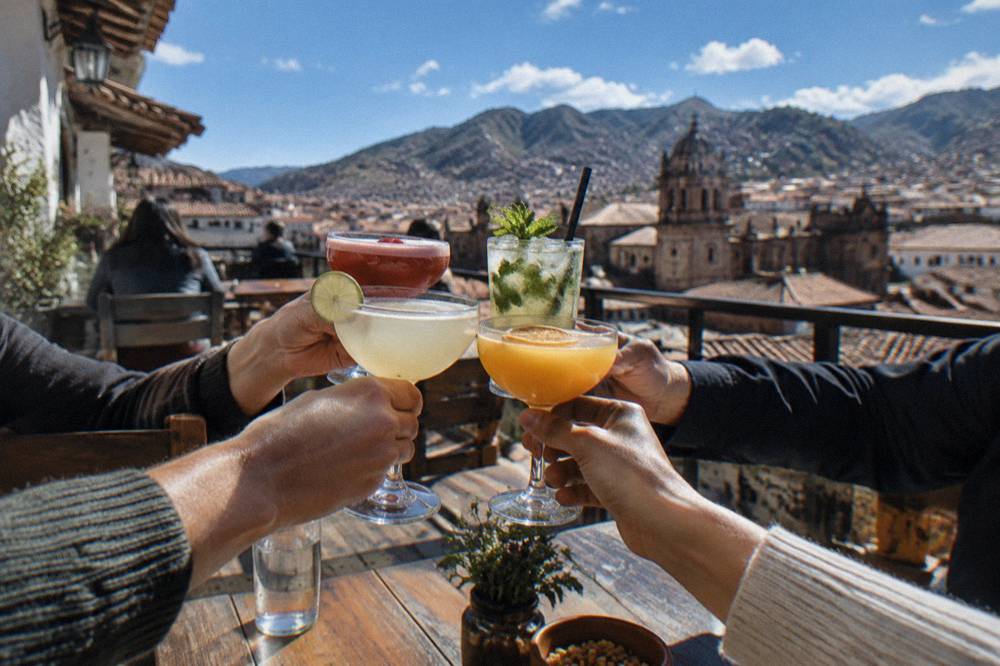 A small group raising cocktail glasses together at a wooden table in a Cusco bar
