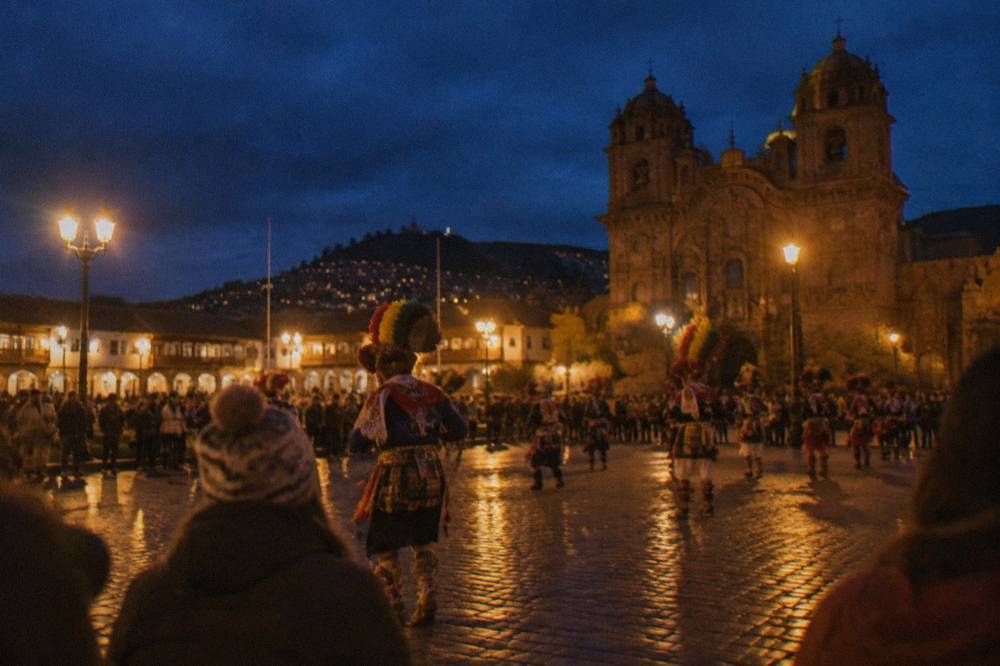 A crowded plaza in Cusco at night with costumed performers and onlookers
