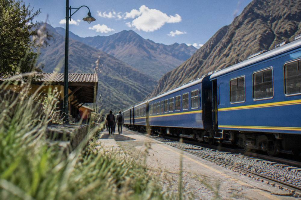 A train waiting at a small Andean station platform with mountains behind