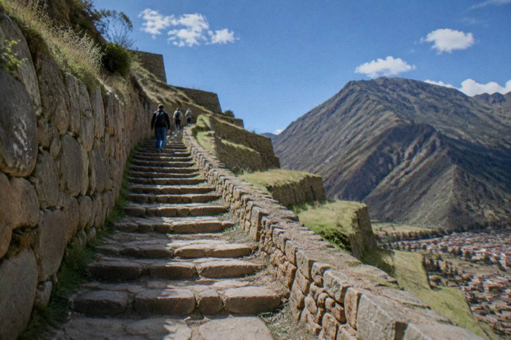 Travellers walking up stone steps between Inca terrace walls in bright daylight