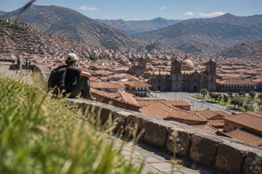A traveller resting on a stone terrace overlooking red-tiled rooftops of Cusco