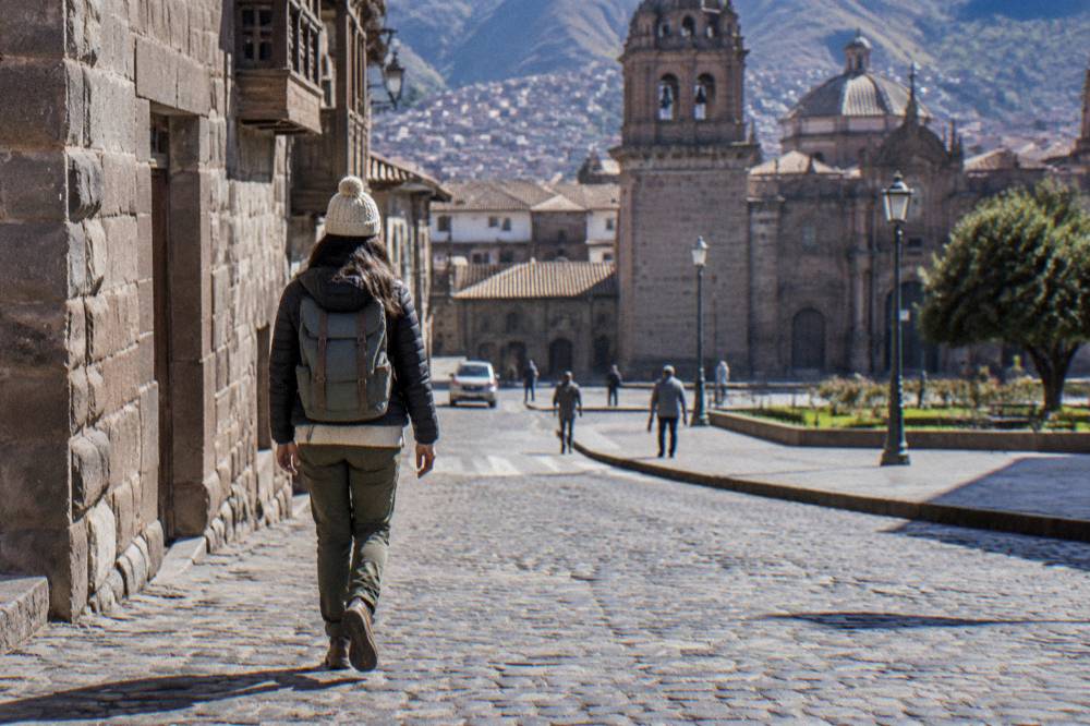 A layered-dressed visitor walking a sunny cobbled Cusco street in cool morning air