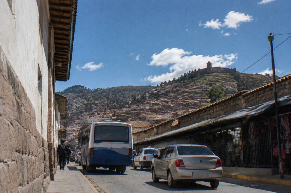 A bus and taxis on a narrow street below Cusco's hillsides