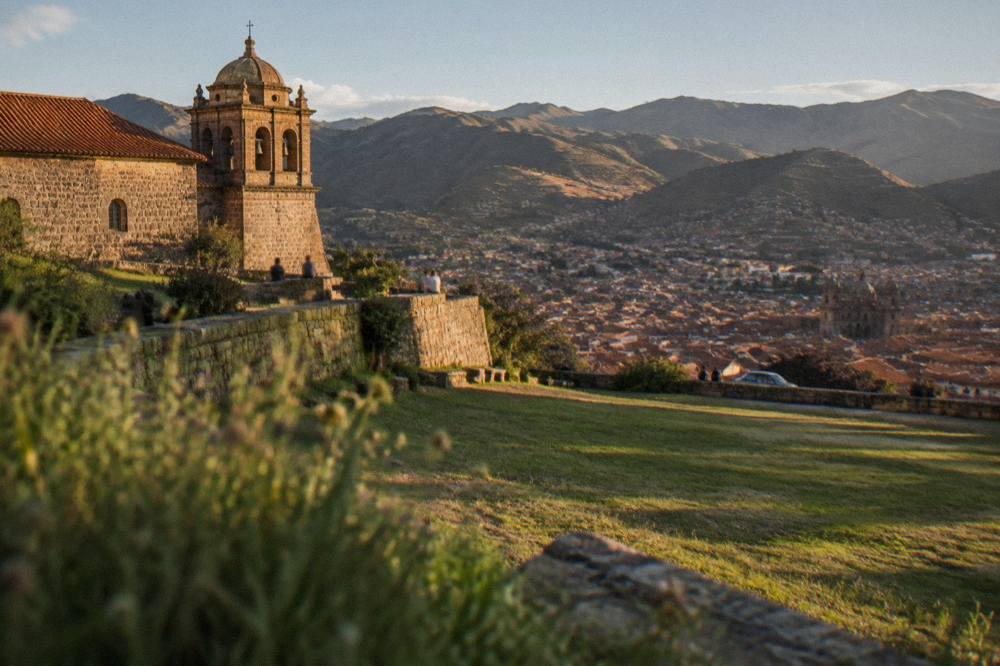 A stone terrace wall above a wide grassed esplanade with the city spread in the valley beyond