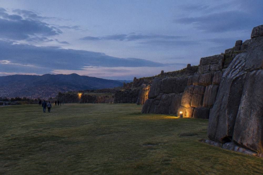 Large fitted stone walls of a terrace with a wide grassy field and hills in the background