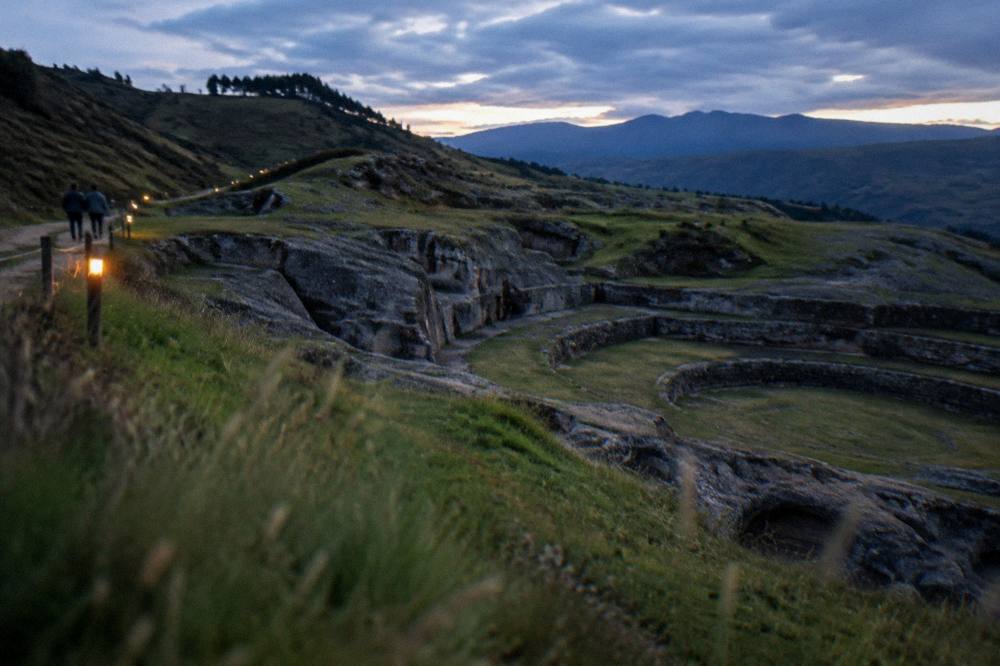 Carved natural rock formations at an archaeological site with grass and hills around