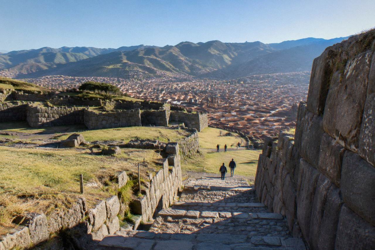 Terracotta roofs of Cusco under a clear blue sky with green Andean hills behind