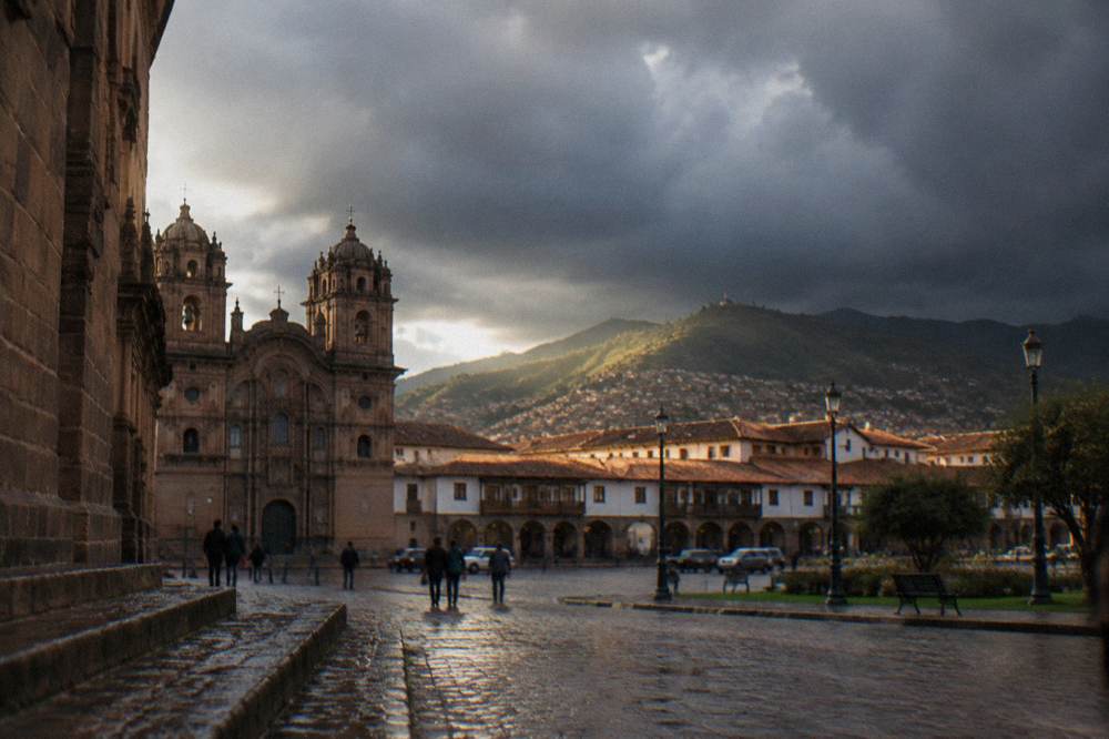 Plaza in Cusco with dark storm clouds gathering over the surrounding hills