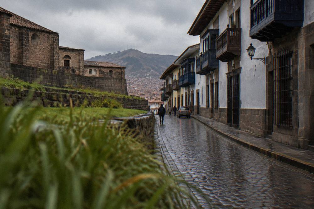 Rain-slicked cobblestone alley in Cusco with colonial balconies above