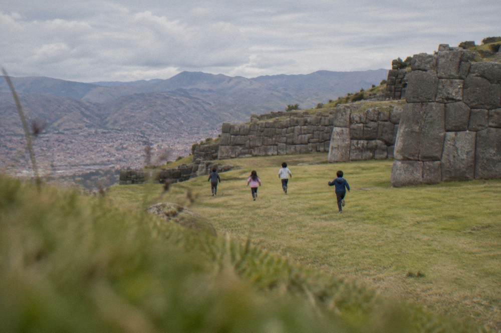 Children running across the open grass terrace at Saqsayhuaman above Cusco