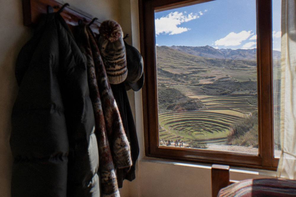 Warm jackets and hats hanging on hooks by a window in a Cusco room
