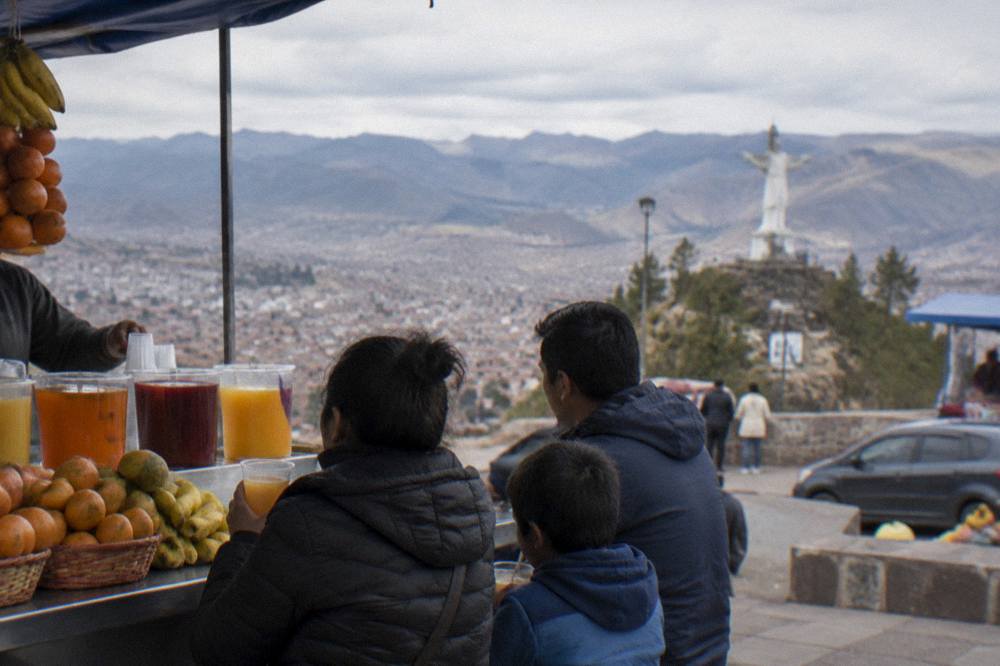 A family sharing fruit juice at a busy market counter in Cusco