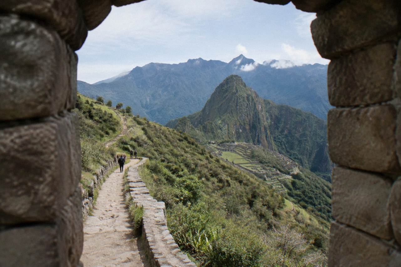 A hiking trail winding across a green Andean ridge above Cusco with terraced hillsides under a clear sky