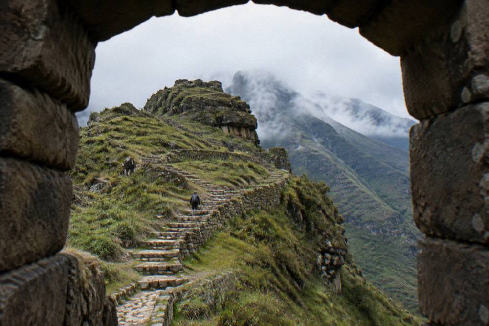 Stone Inca staircases climbing a green mountainside toward a cloud-wreathed pass