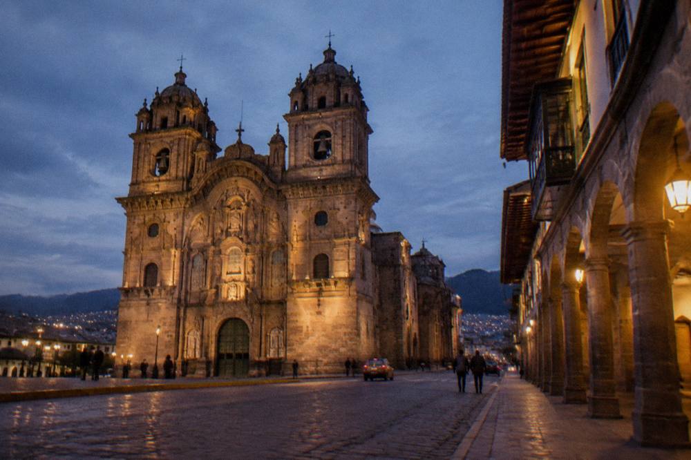 A street in Cusco at dusk with lit doorways and stone arcades