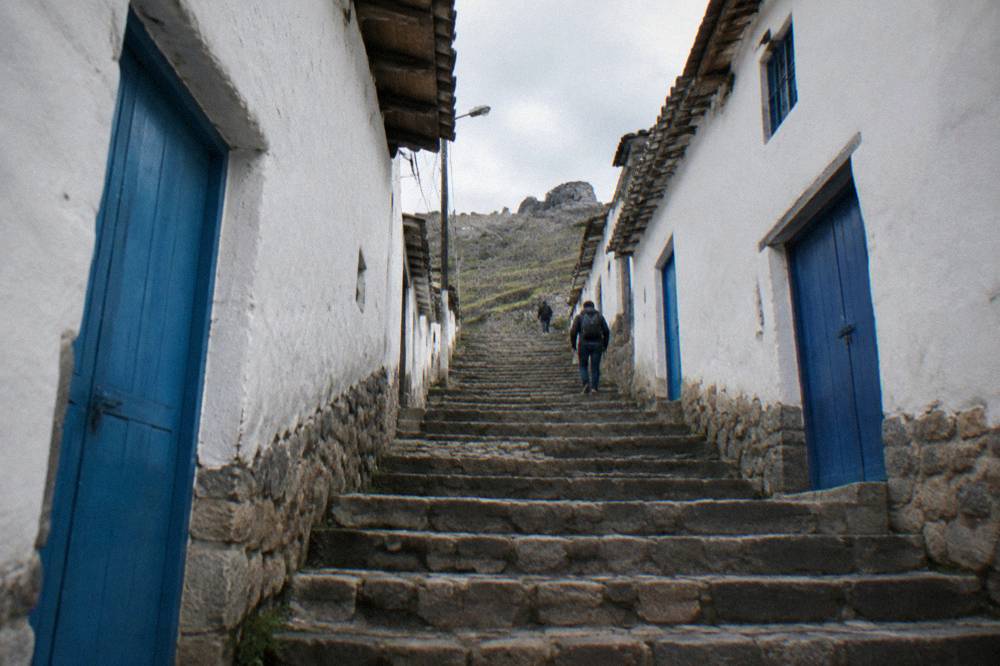 A steep pedestrian stone staircase in Cusco lined with whitewashed walls and blue doors