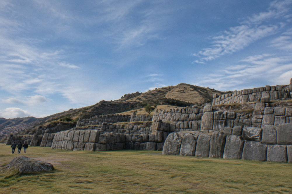 The terraced stone walls of Sacsayhuaman under a wide blue sky with hills behind